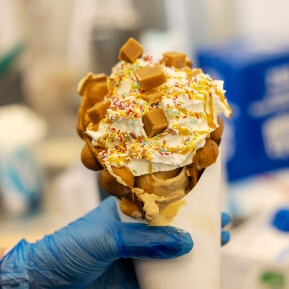 image of an ice cream waffle cone, topped with fudge pieces and sprinkles