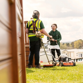 Image of a man with a lawnmower, talking to another man in the holiday park
