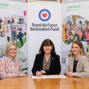 Image of three women sat at a table signing an agreement with a royal air force banner behind them