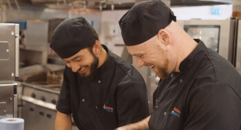Image of 2 chefs smiling while cooking in a kitchen