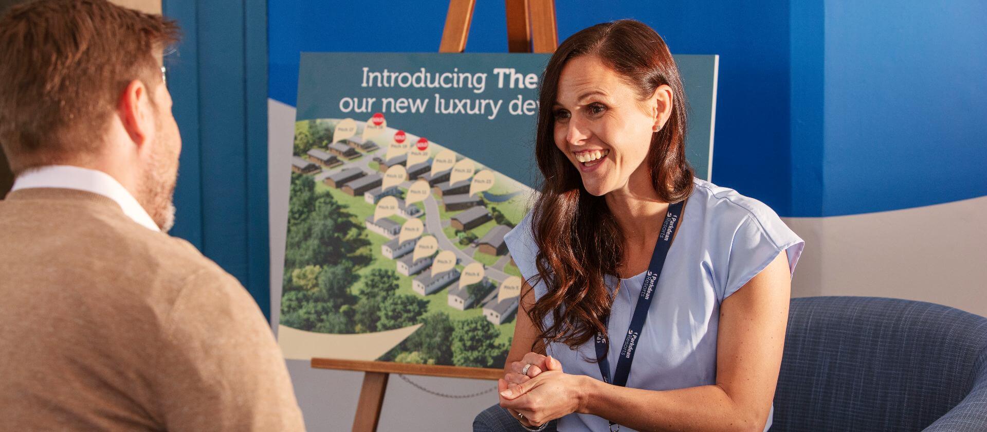 Image of woman mid conversation with a man, holiday home sales board is in the background