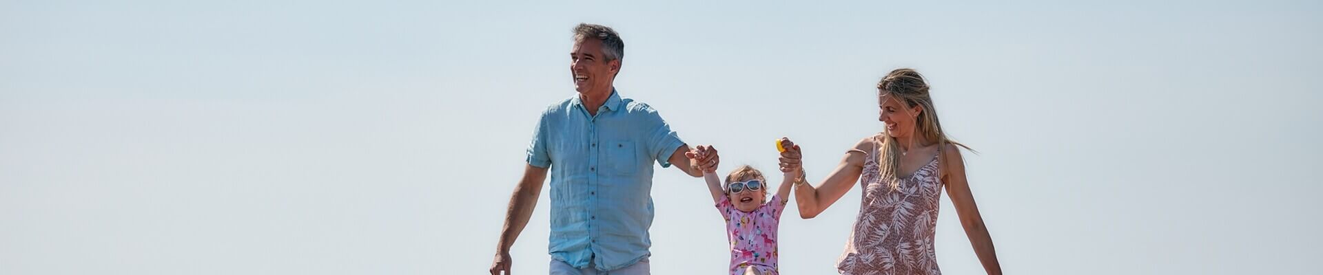 Image of two adults holding hands with a little girl on the beach