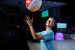 A woman in a light blue t-shirt, throwing a beach ball into the air.