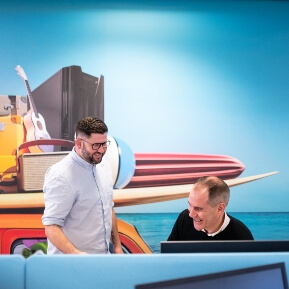 image of a man sitting behind a desk smiling with another man stands smiling next to him