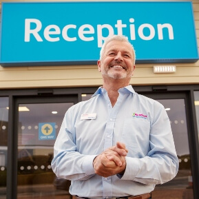 image of a manger, smiling and clasping his hands as he waits in front of the hotel reception