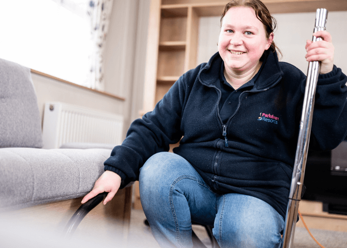 A woman knelt on the floor whilst hoovering by a sofa