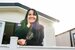 A lady in a suit jacket and leopard print top leaning on a fence in front of a holiday home smiling.