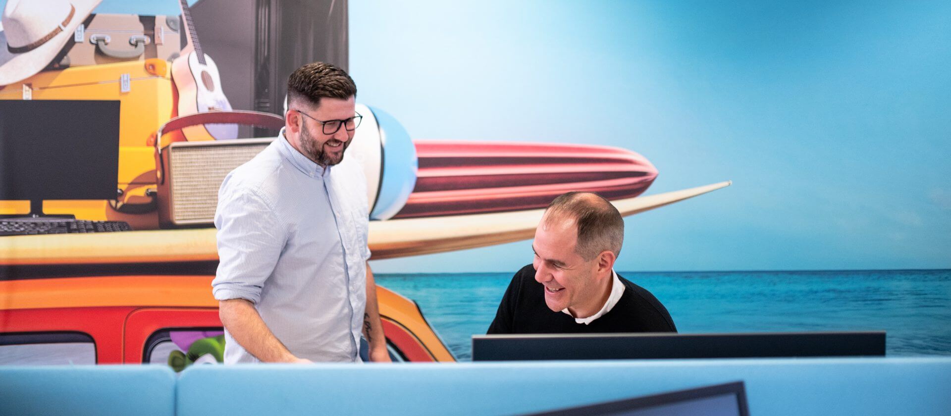An image of two men chatting while looking at a computer screen.