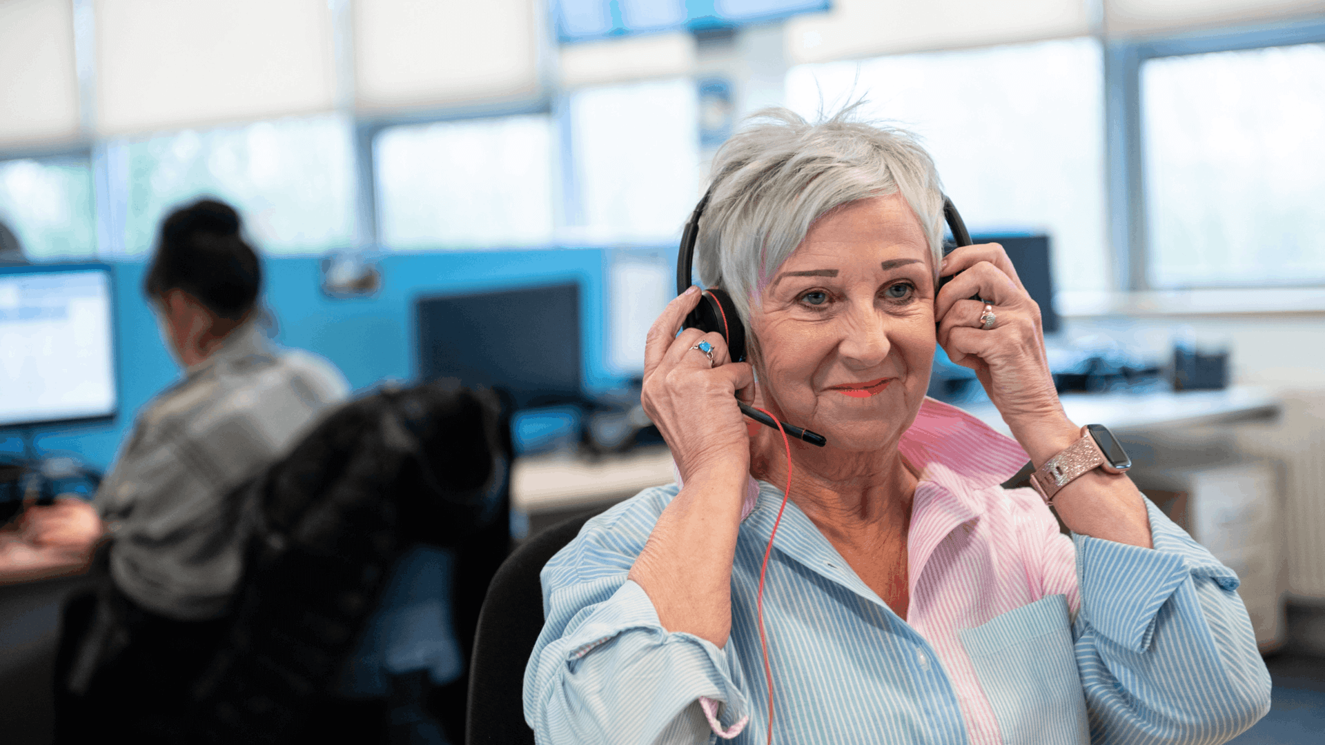 A woman wearing a light blue blouse in an office wearing a headset
