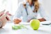 Healthy food concept. Cropped close up of woman doctor dietician recommending senior male patient fresh apple.