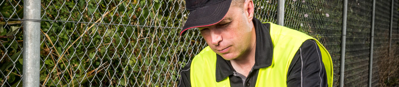 Technician in a yellow vest next to a fence