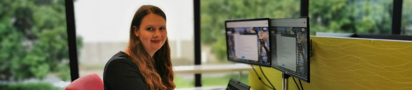 Woman sitting in an office in front of a computer screen looking into the camera
