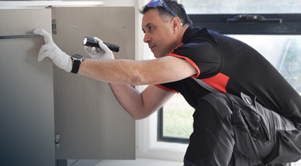 Pest technician kneeling down to service kitchen