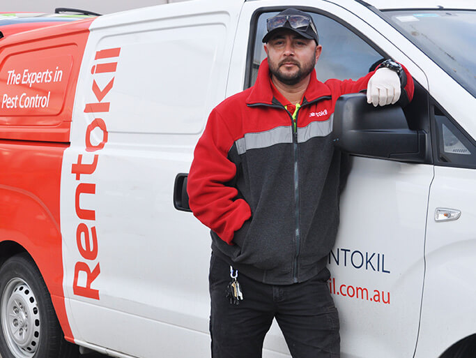 Pest technician leaning on his van