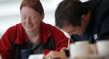 Two employees smiling and writing something down at a training session