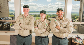 Three Western Exterminator employees stand with crossed arms in front of a large window that shows a vast landscape.