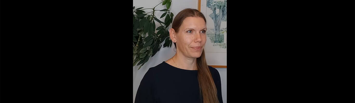 En midaldrende blond kvinde med blå øjne og en sort top kigger til højre.