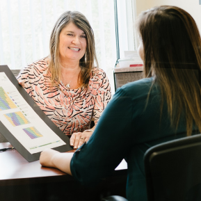 Two smiling women sit at a table, one of them holding a diagram.