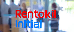 Das "Rentokil Initial"-Logo stehen verschwommen im Vordergrund eines unscharfen Bildes von Menschen in einem Geschäft.