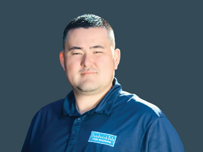 A headshot of a smiling man in a blue Sandwich Isle Pest Solutions polo shirt against a dark blue background.