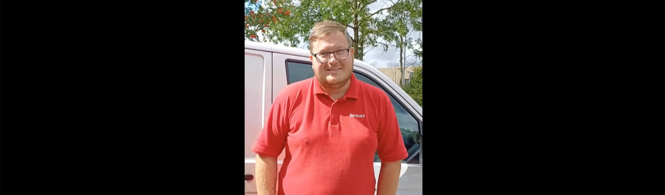 En mand med briller og skæg smiler og har en rød Rentokil-poloshirt på. En hvid varevogn kan ses i baggrunden.