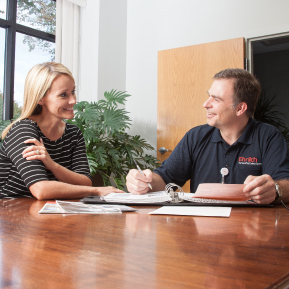 An Ehrlich employee in a blue shirt sits at a wooden table with a smiling blonde woman, both looking at each other.