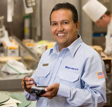 Steritech technician smiling to the camera in a kitche with handheld device