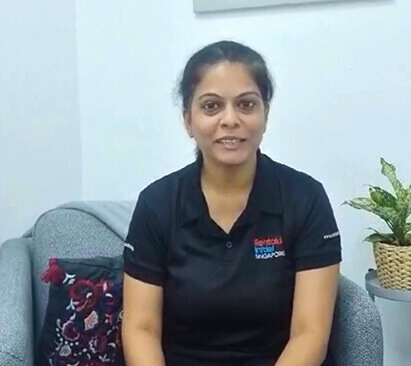 A smiling woman is sitting on a grey sofa in a black Rentokil uniform.