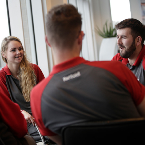 Three smiling Rentokil employees chat while sitting together in a modernly lit room.