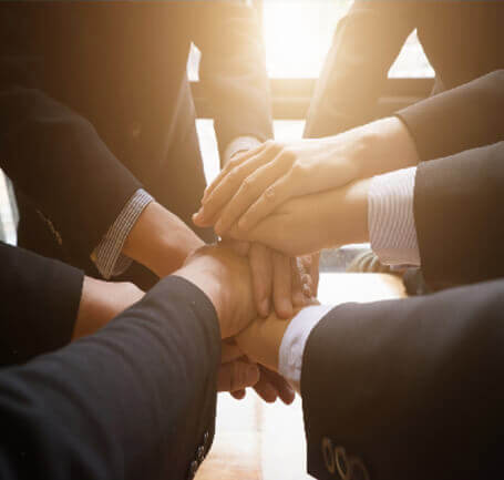 A group of people, all wearing formal attire, place their hands together in a circle in the middle.