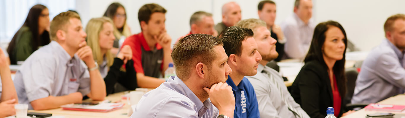 A row of people, some with their chins in their hands, are sitting and attentively listening during a presentation or meeting.