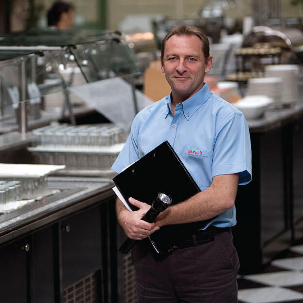 A smiling, middle-aged white man stands in a catering area holding a black folder.