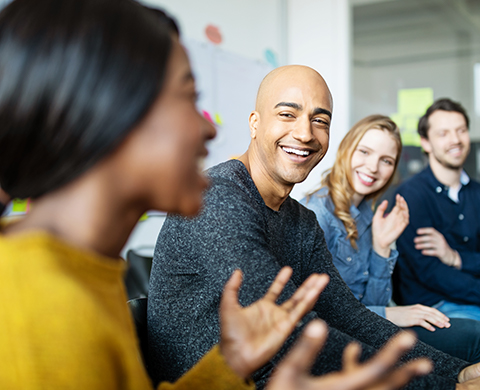 Alt text: A smiling young bald man in the foreground looks at another person with a big smile.