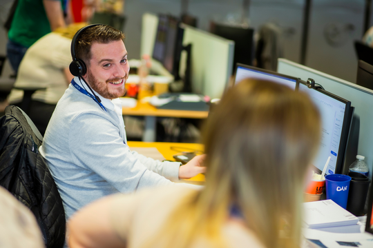 man in headset at a computer smiling at his colleague