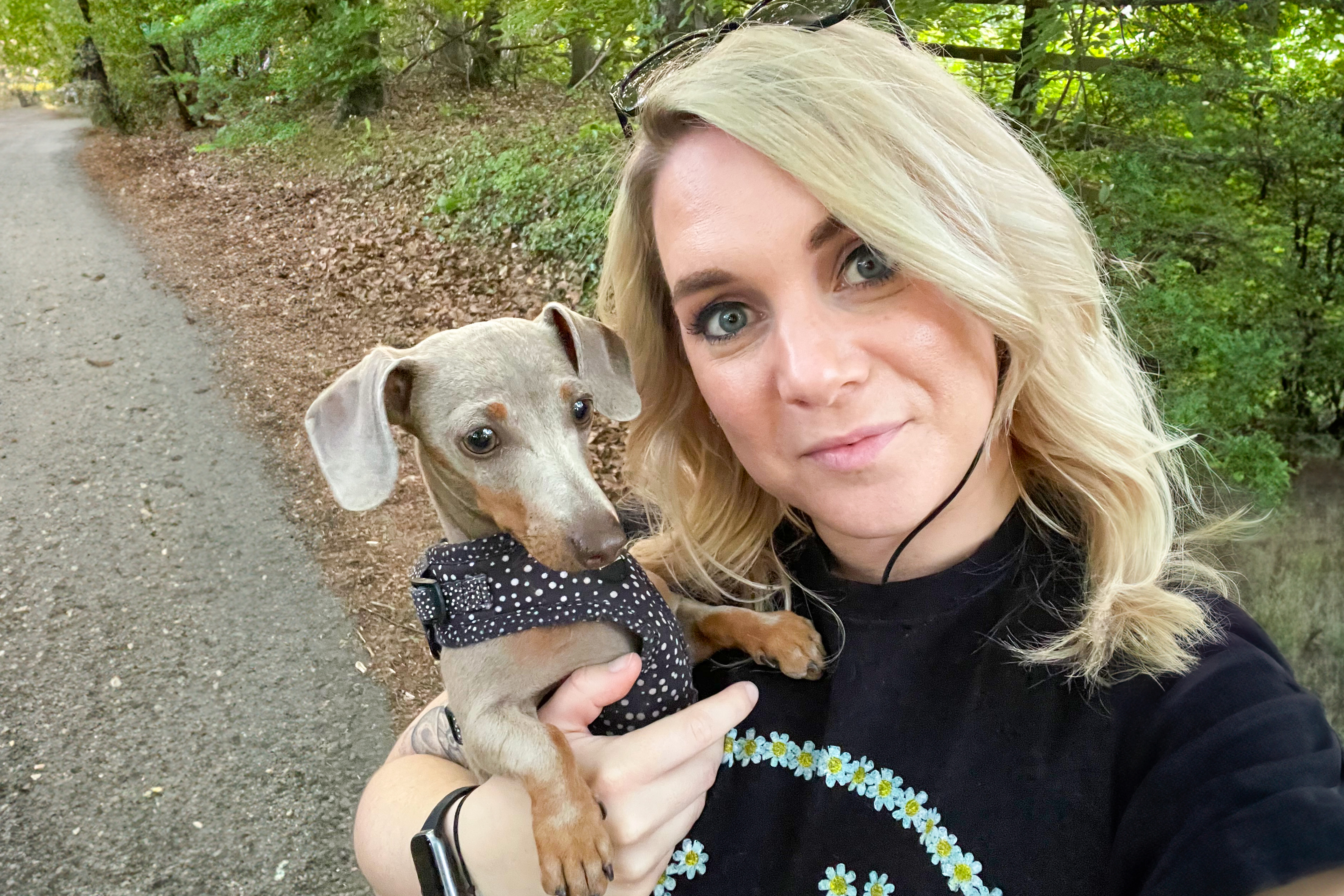 Photo of Gemma, in the woods, holding her pet dog and smiling while taking a selfie.
