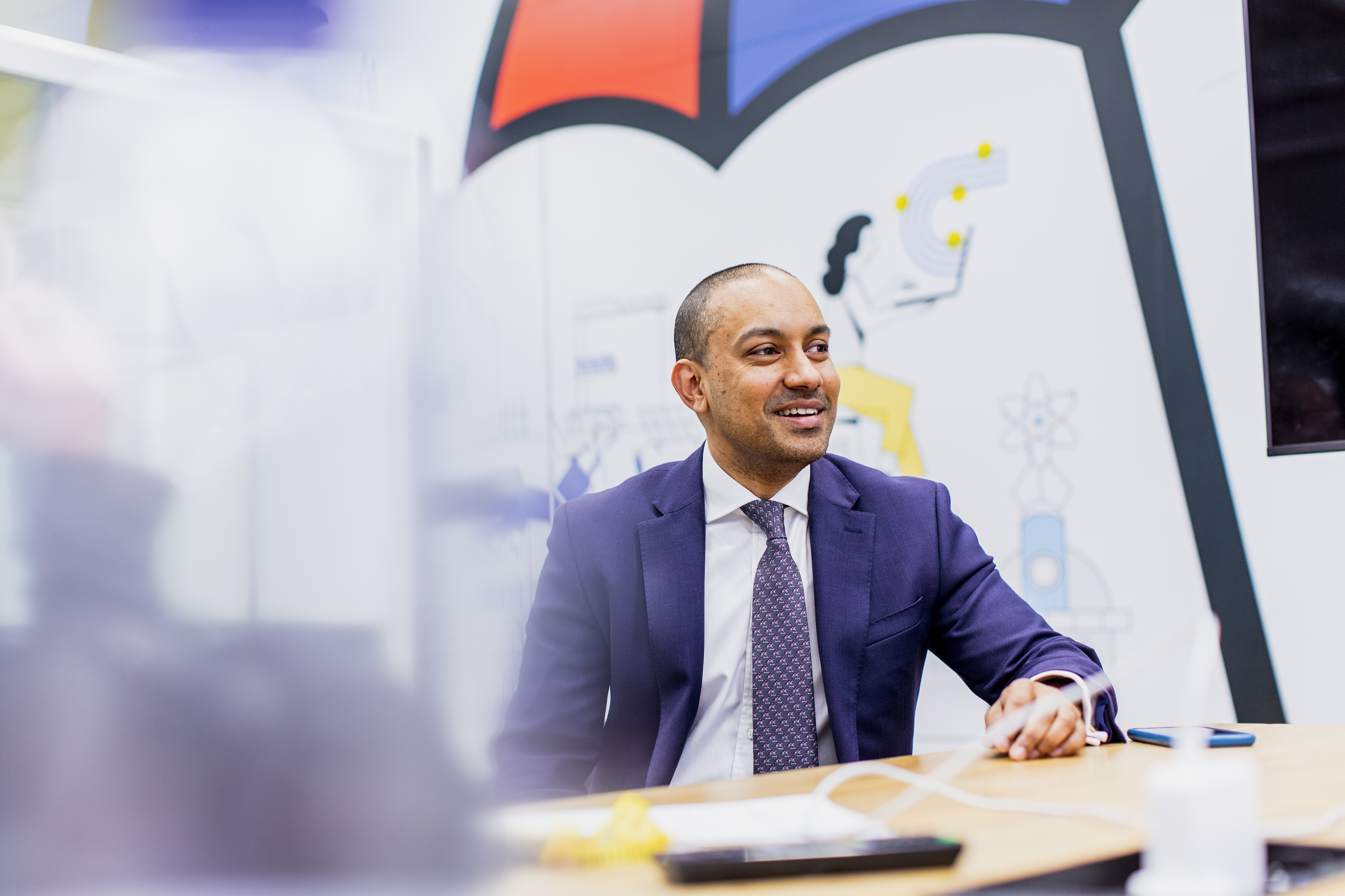 man smiling sitting at desk in suit and tie