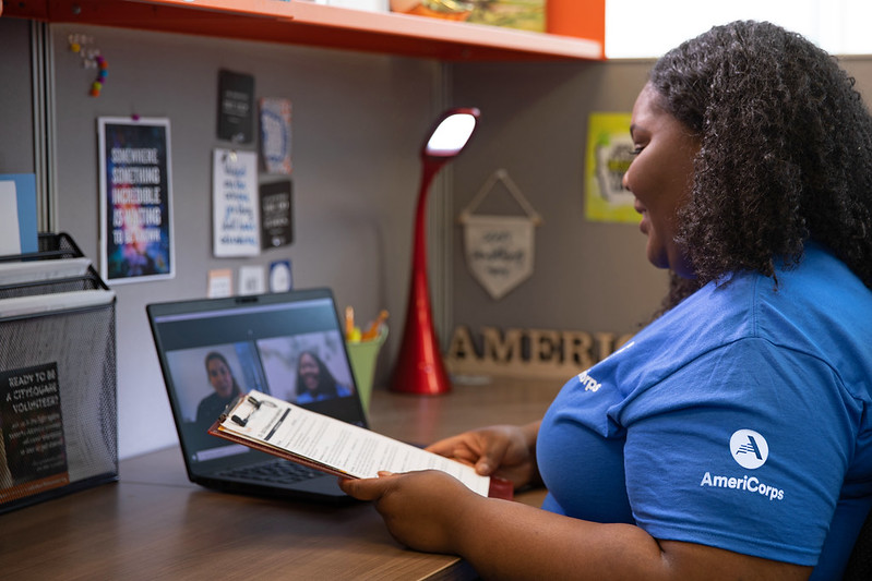 Photo of women working at a computer with a clipboard and wearing an AmeriCorps t-shirt.