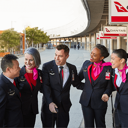 Several Qantas Cabin Crew members from diverse cultural backgrounds smiling and engaging with each other outside the terminal, highlighting team camaraderie and inclusivity.