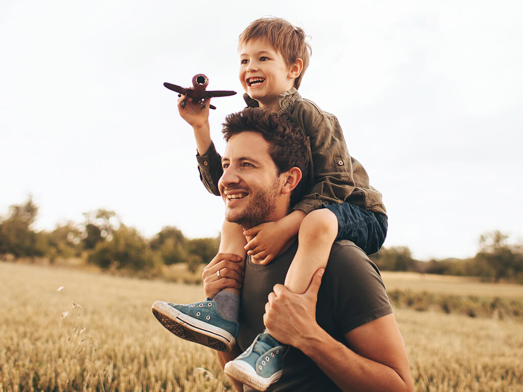 A father and son playing with a toy plane in a field