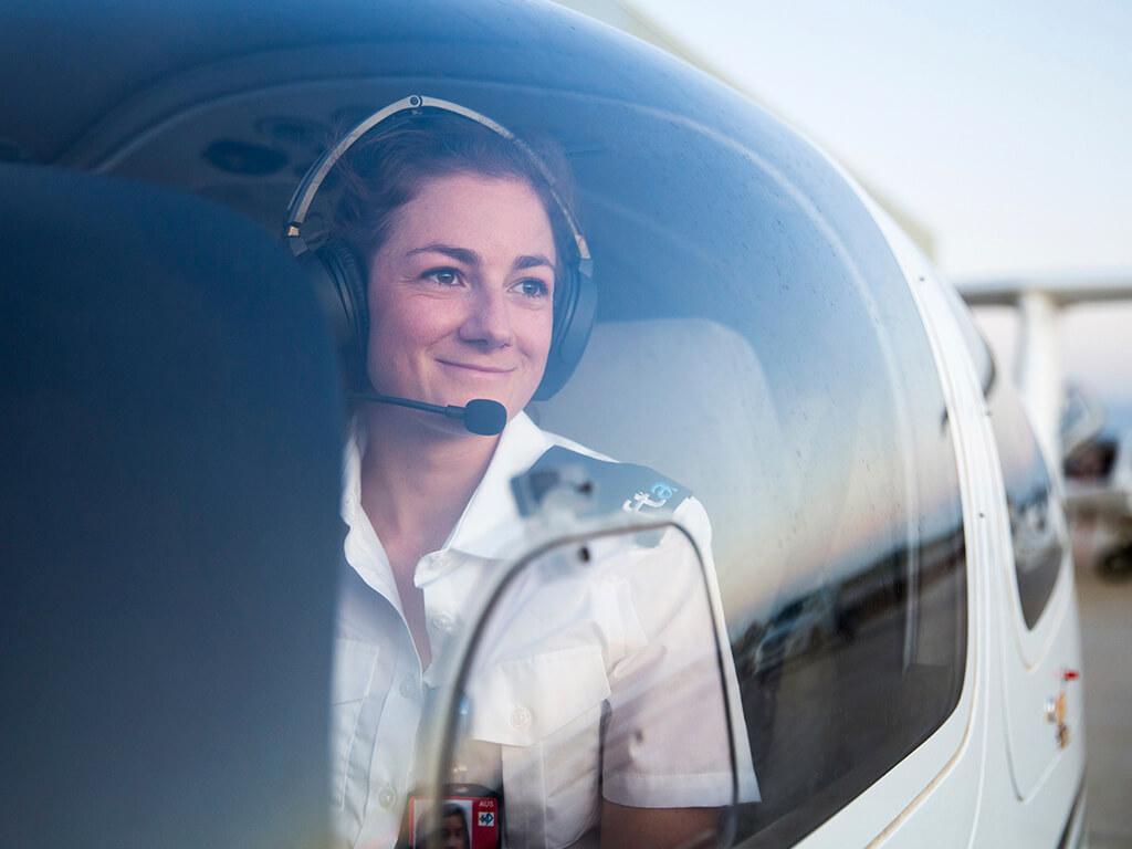 Trainee from the Qantas Group Pilot Academy smiling and looking out of a cockpit window, showcasing enthusiasm and training in aviation.