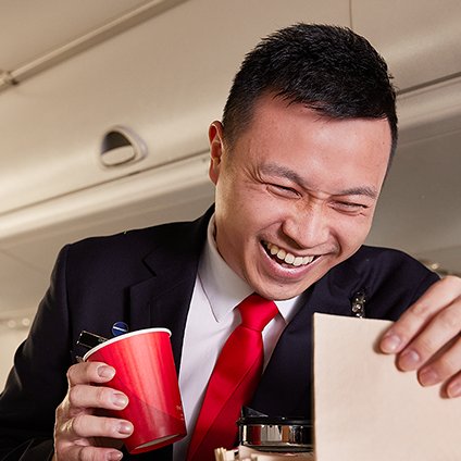 A member of our cabin crew team laughing while serving customers on a flight