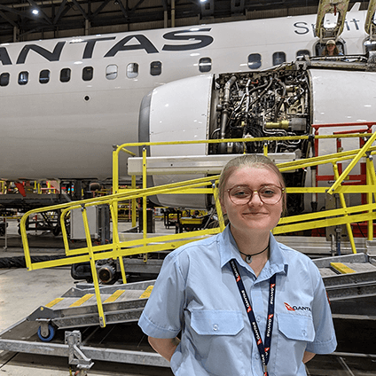 An engineering apprentice in the hangar, smiling at the camera