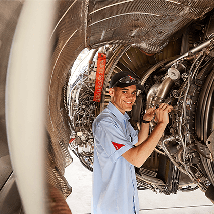 An engineering apprentice working on the mechanics of a plane, smiling at camera