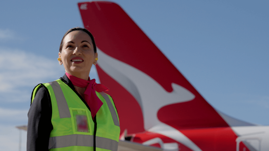 Customer Service Agent wearing high-vis uniform on tarmac in front of a Qantas aircraft