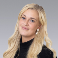 a headshot of a blonde woman in a blue suite jacket smiling at the camera