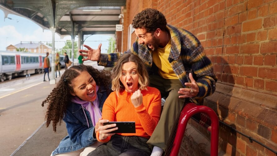 Image of three people looking at a cellphone in excitement  