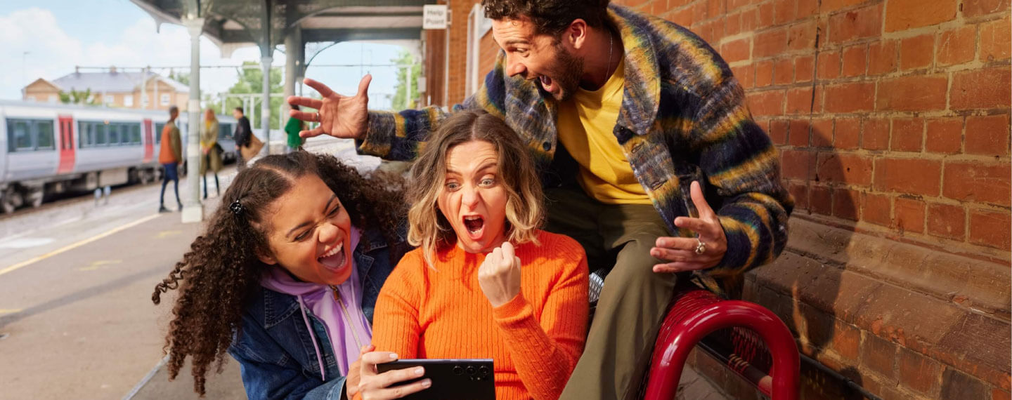 An image of three people looking at a cellphone in excitement 