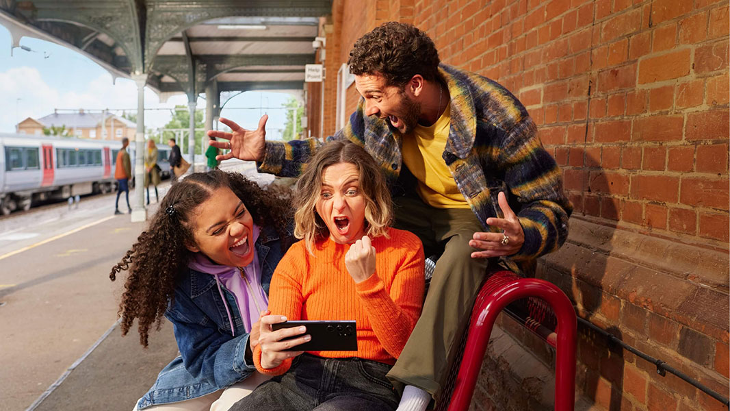 Image of three people looking at cellphone in excitement 