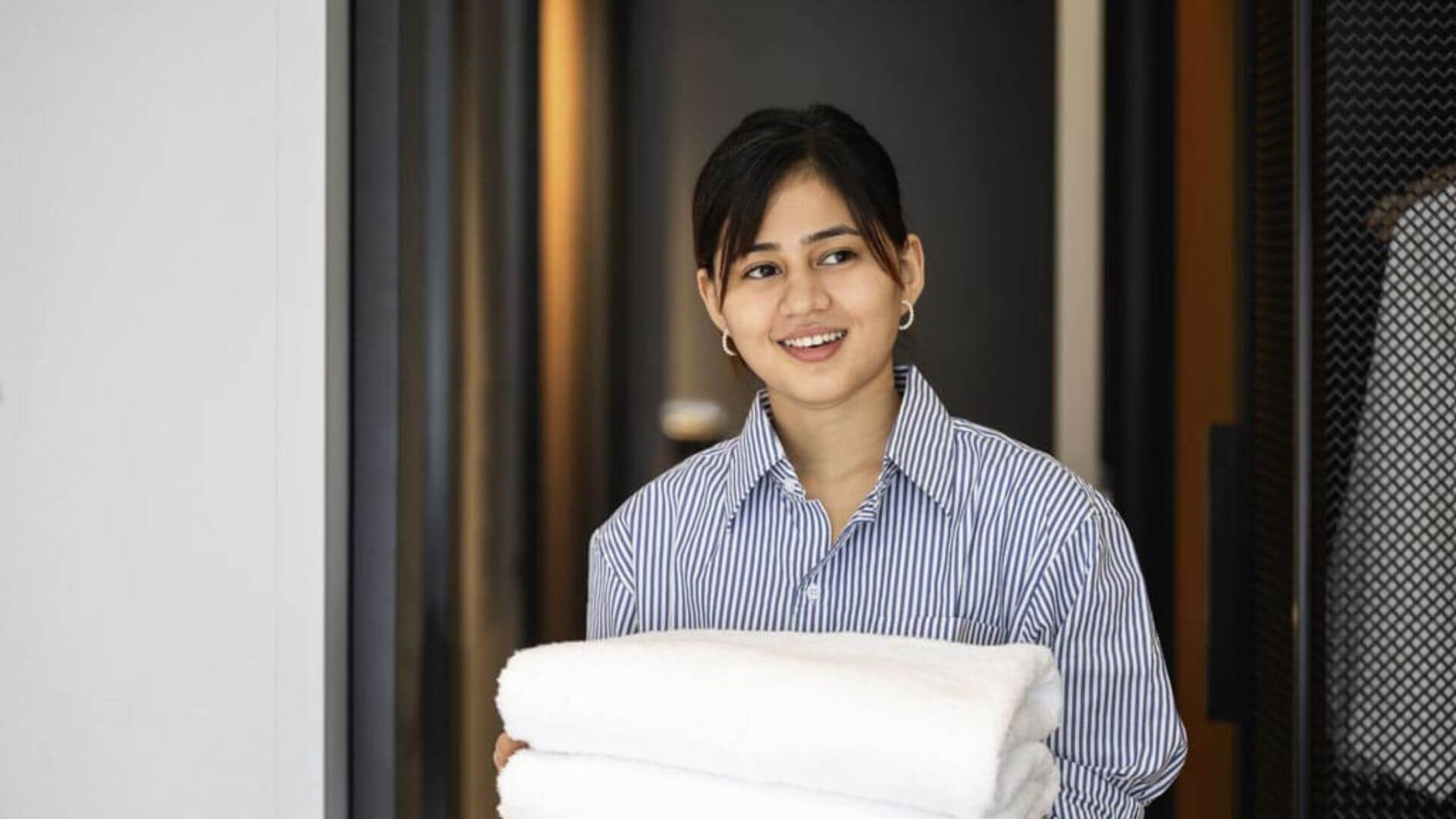 housekeeper with blue shirt holding towels and smiling 