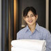 Gouvernant(e) portant une chemise bleue, tenant des serviettes et souriant.